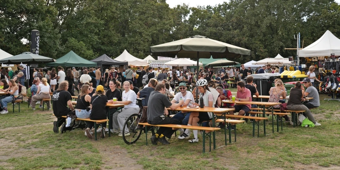 © Elisabeth Els Menschen auf Bierbänken, die ihr Essen beim Veganmania Streetfood Festival genießen.