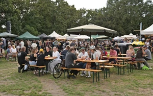 Menschen, die beim Veganmania Streetfood Festival auf Heurigenbänken sitzen und ihr Essen genießen.