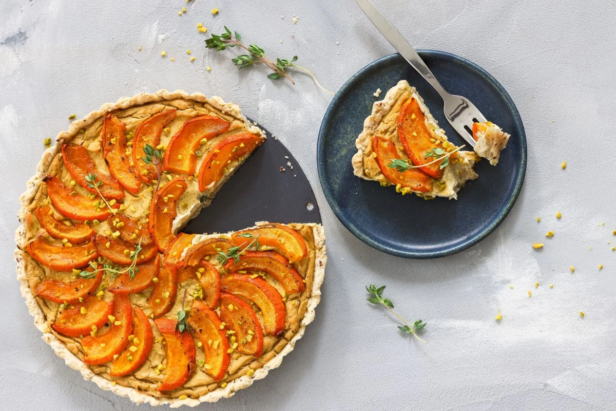 angeschnittene Tarte, die mit Kürbisscheiben belegt ist, und daneben ein Teller mit einem Stück der Tarte