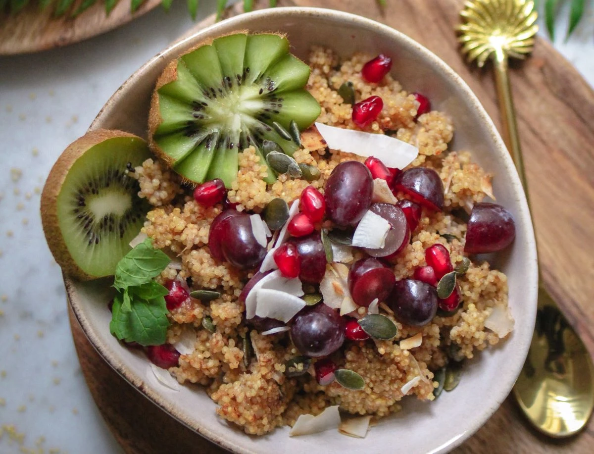 Bowl mit Hirse als Grundlage und Weintrauben, Granatapfelkernen, Kiwi und Kokosraspeln als Toppings