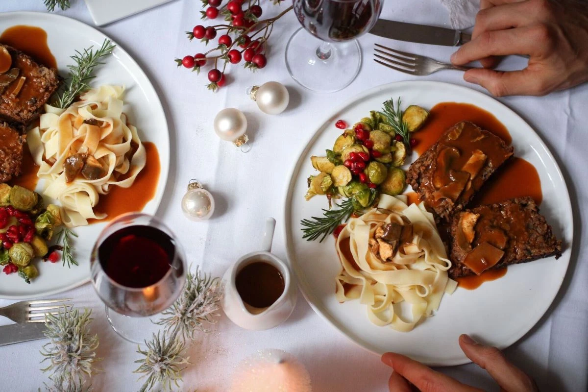 zwei Teller mit veganem Braten, Tagliatelle und Kohlsprossen auf einem festlich gedeckten Tisch