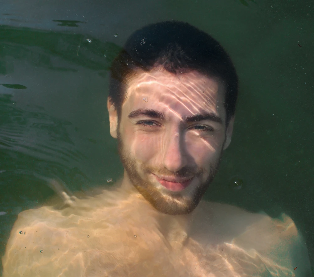 Junger Mann blickt von unter dem Wasserspiegel empor